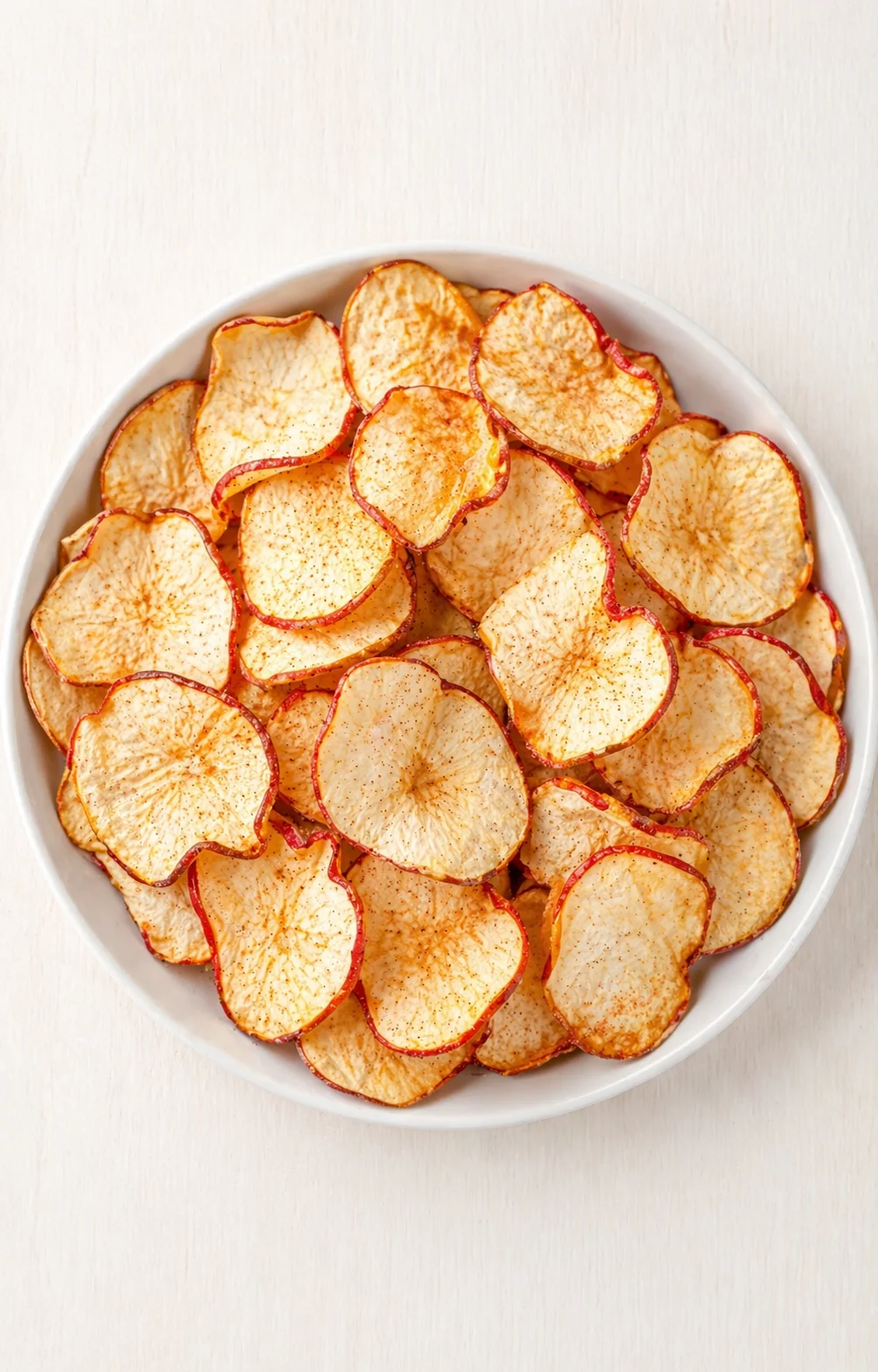 White bowl filled with dried apple slices on a light wooden table