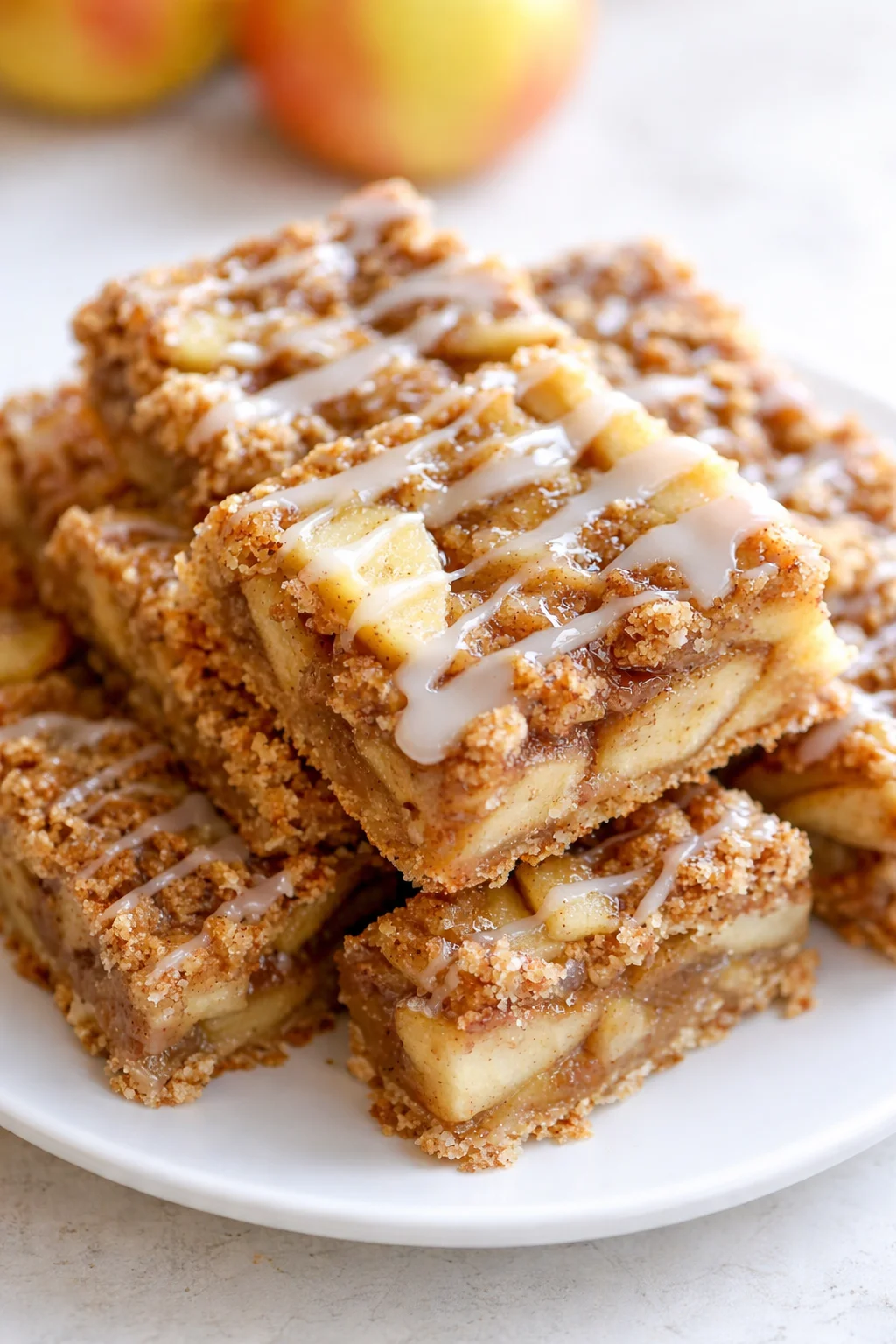 Stack of apple crumble bars with crumb topping and white icing on a plate.