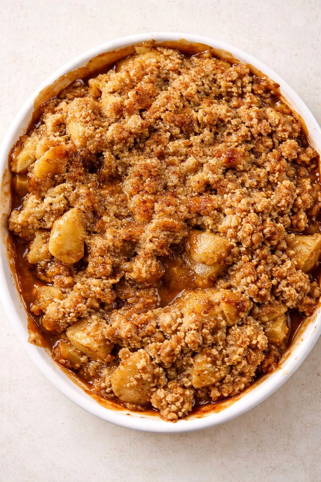oval white baking dish filled with golden-brown apple crumble, caramel sauce around edges