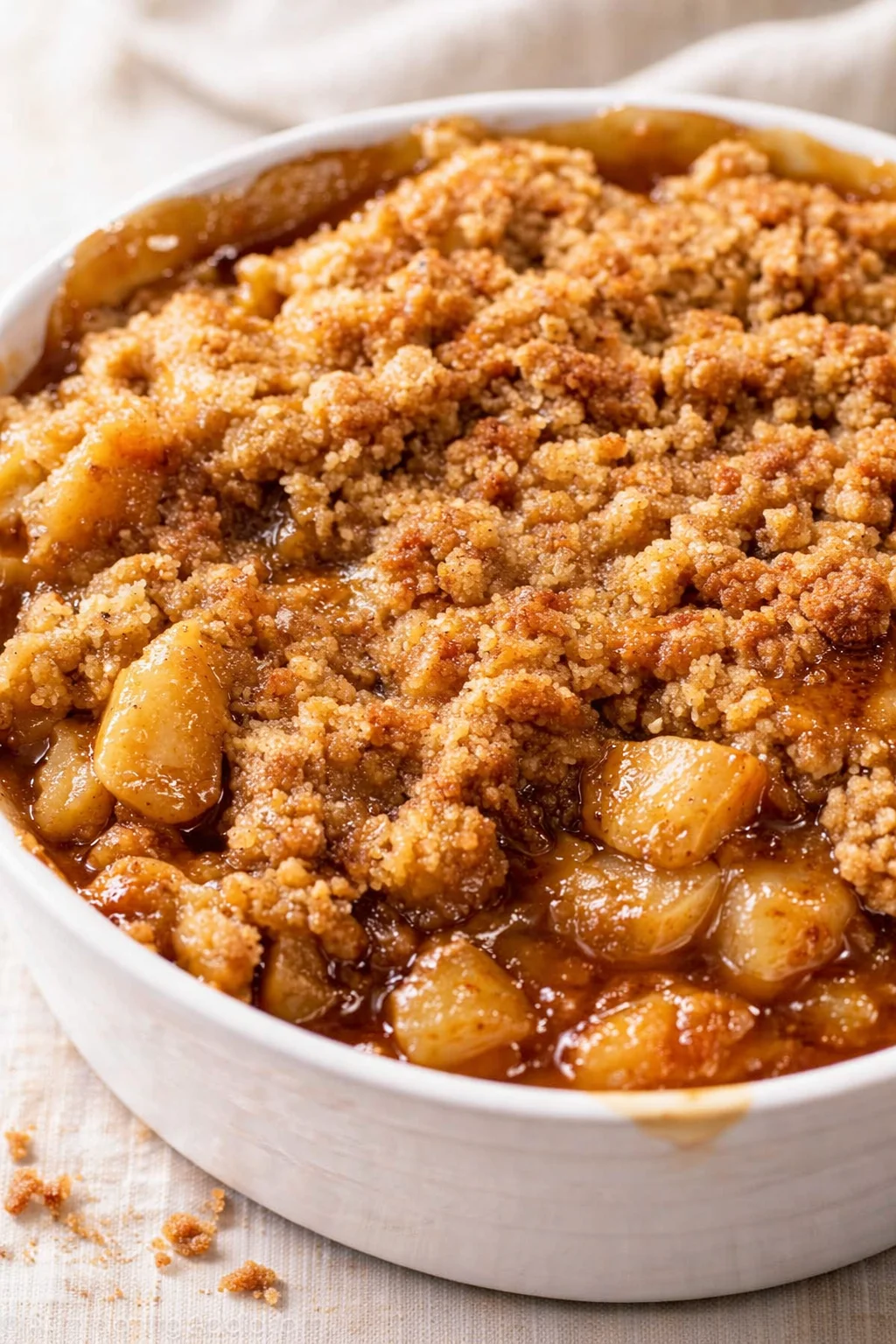 white baking dish filled with golden-brown apple crumble and glossy caramel sauce