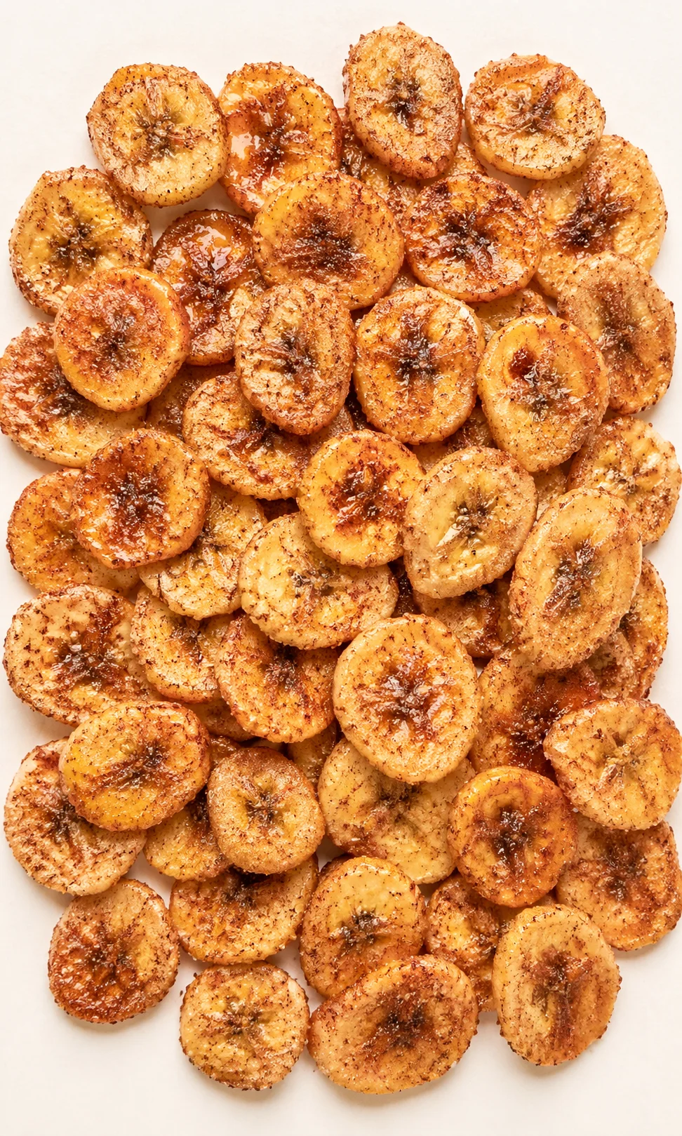 Piled caramelized banana chips with cinnamon sugar on a light background.