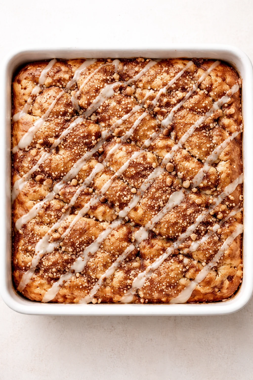 golden braided cinnamon bread in a white baking dish with white glaze drizzle