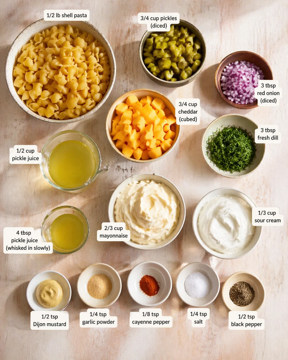 Top-down view of bowls with shell pasta, diced pickles, cheddar, onion, dill, and creamy sauces.
