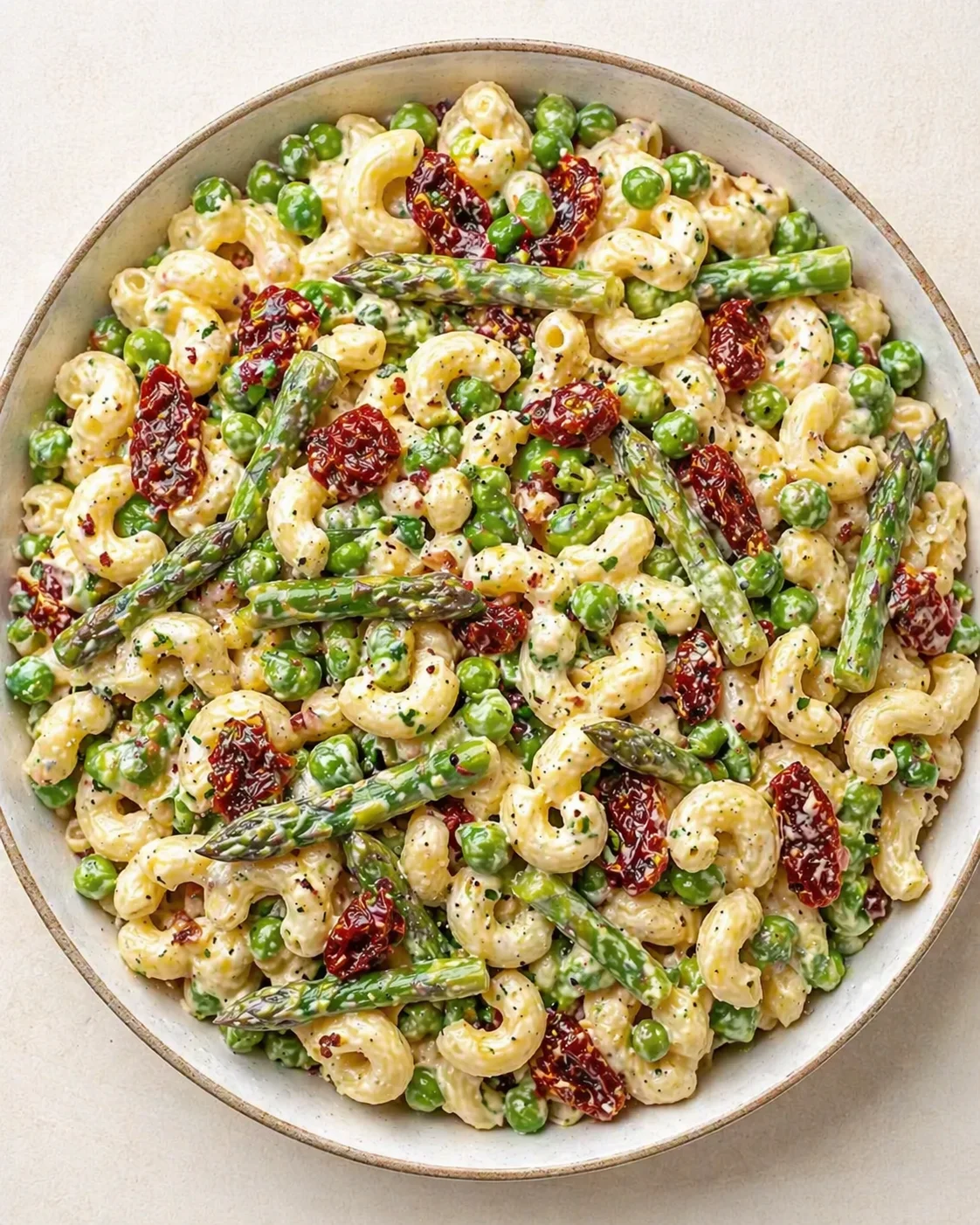 Creamy pasta with peas, asparagus, and sun-dried tomatoes in a light bowl.