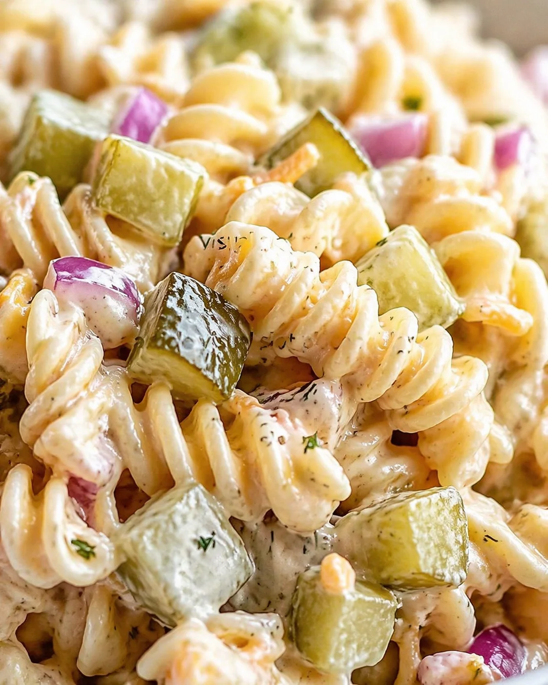 Close-up of creamy pasta salad with rotini, cucumber chunks, red onion, and herbs.