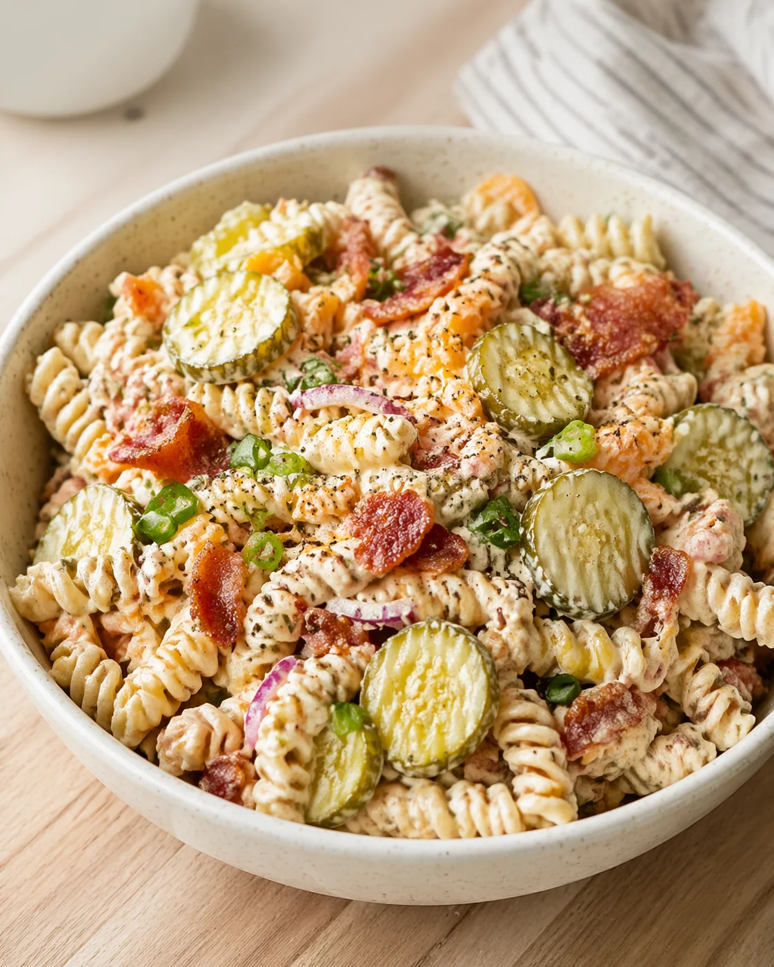 bowl of creamy pasta salad with fusilli, pickle rounds, bacon, red onion, and green onions