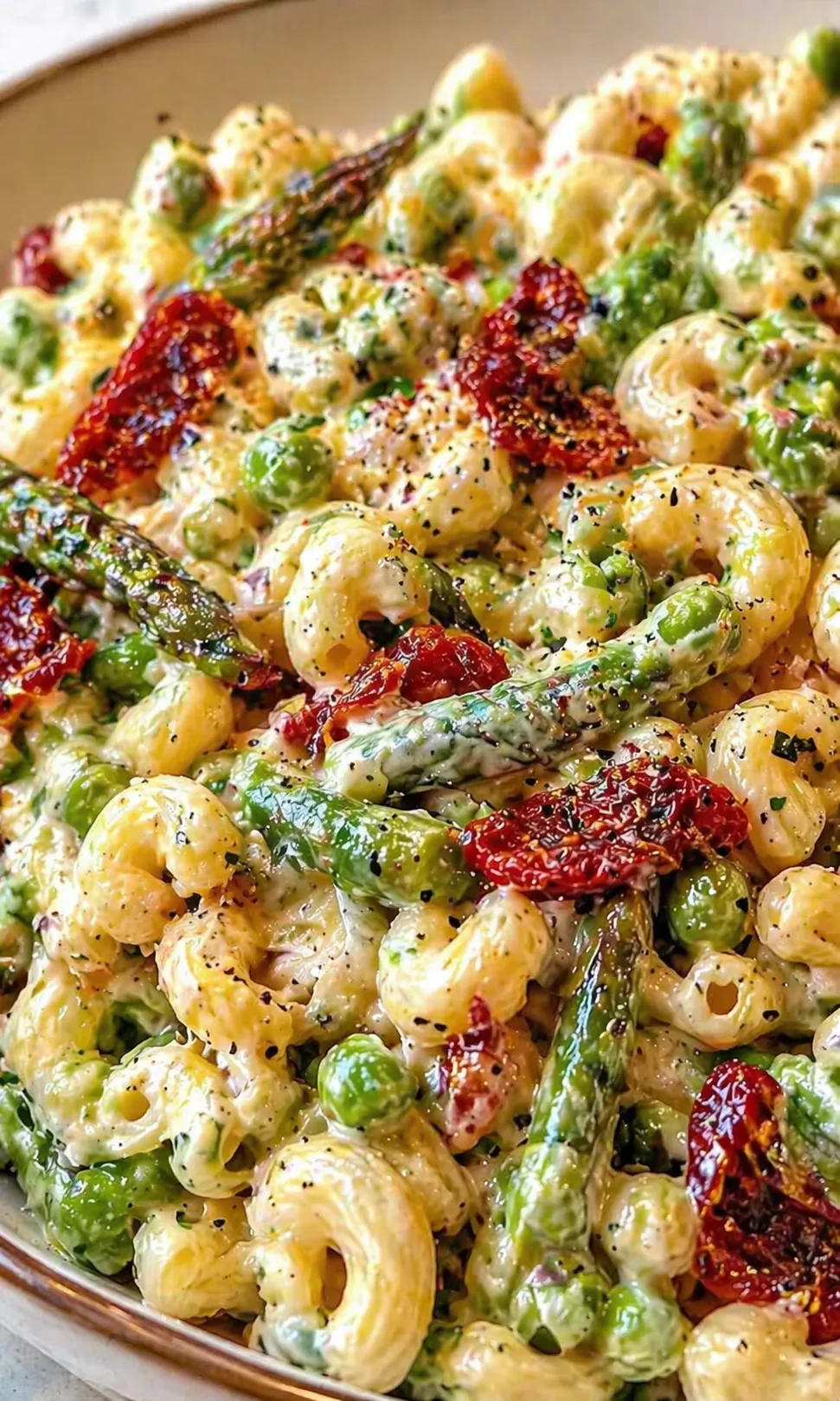 Creamy pasta shells with green peas, asparagus, and sun-dried tomatoes in a skillet