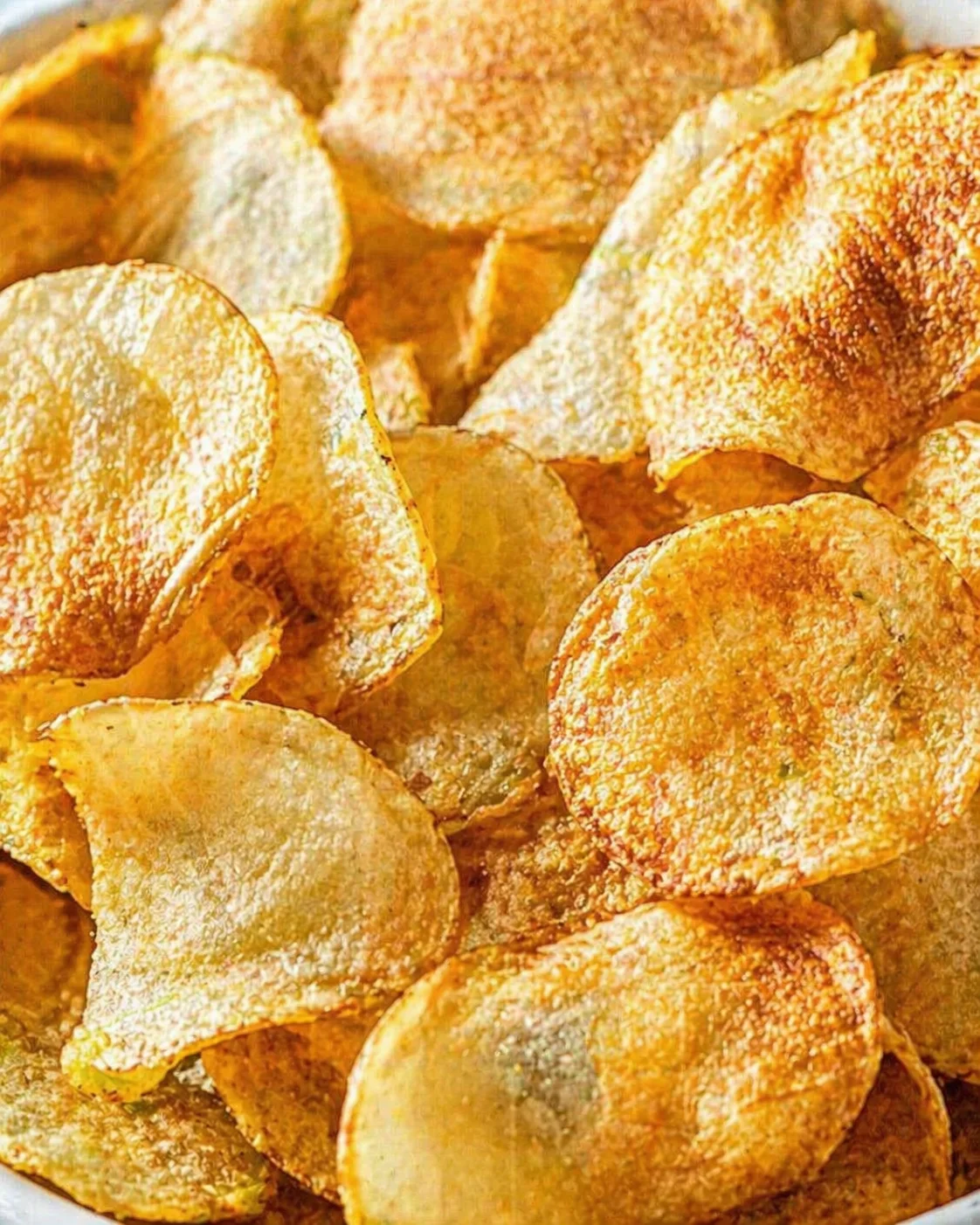 Close-up of golden-brown potato chips, salted and crispy, stacked in a bowl.