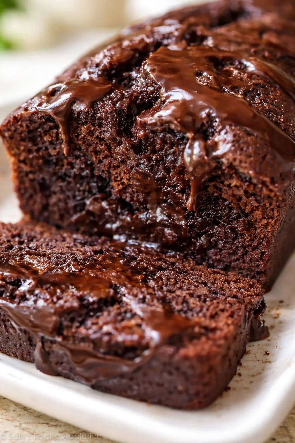 close-up of a fudgy chocolate loaf cake with glossy glaze on a white dish