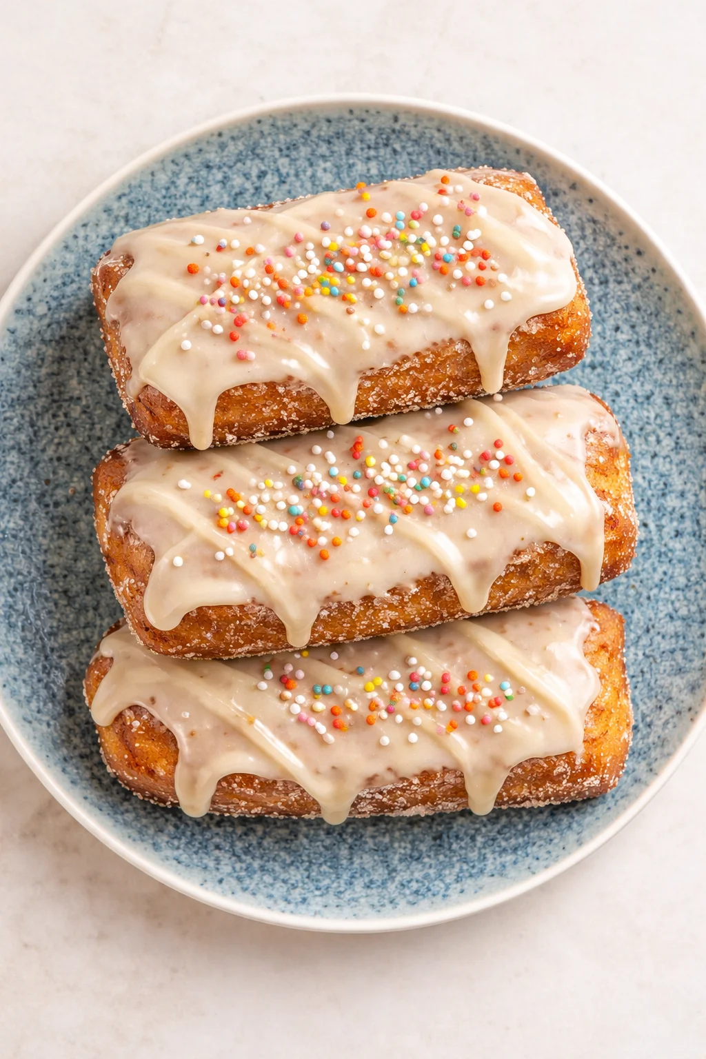 Three rectangular donuts with white glaze and colorful sprinkles on a blue plate.