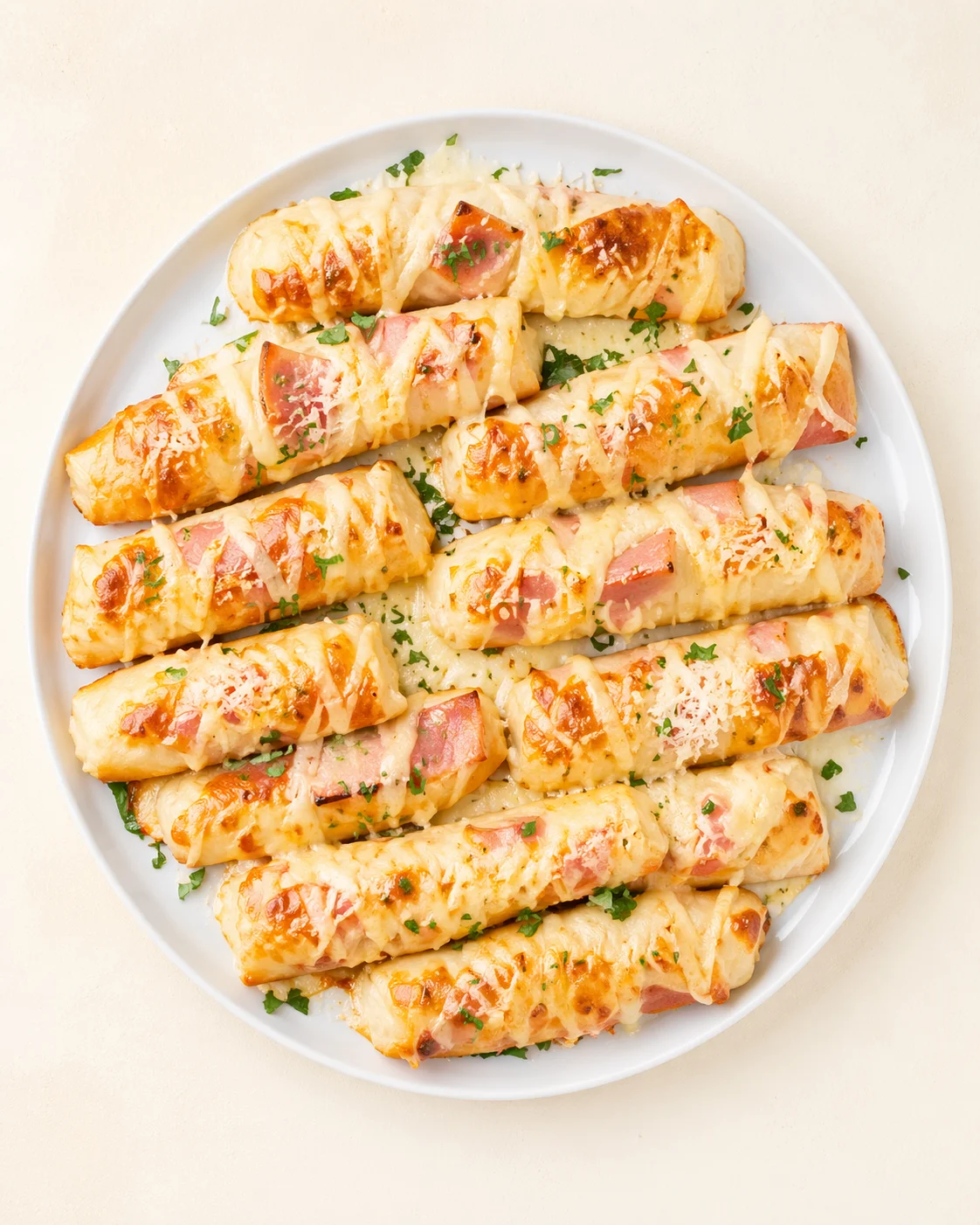 Golden-brown baked ham and cheese pinwheels on white platter, garnished with parsley.