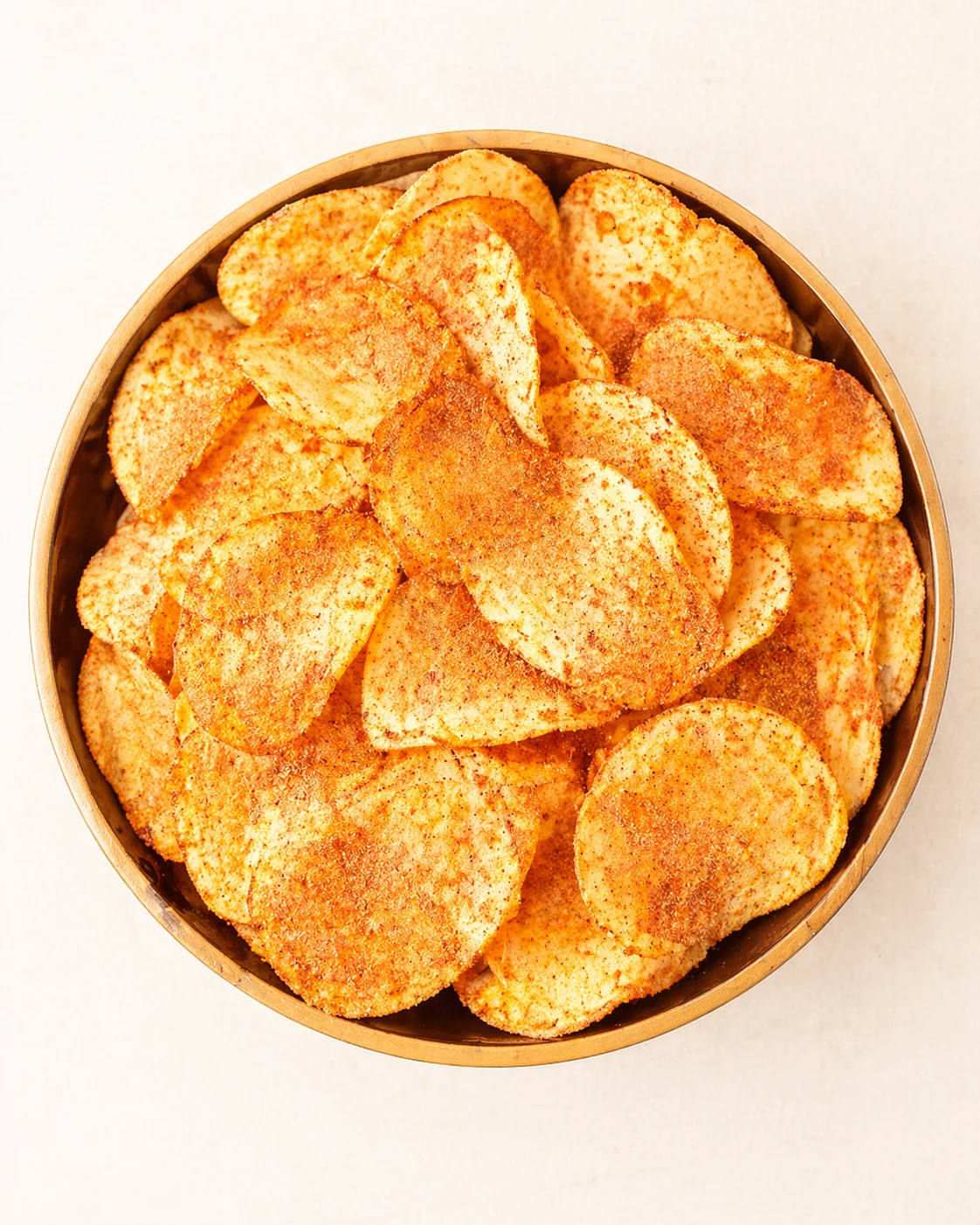 top-down view of a wooden bowl filled with golden, paprika-seasoned potato chips