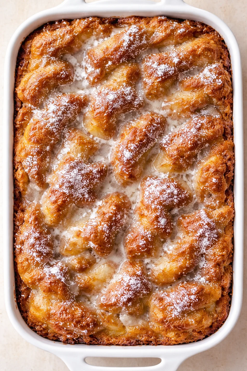 Golden-brown monkey bread chunks in a white baking dish, lightly dusted with powdered sugar.