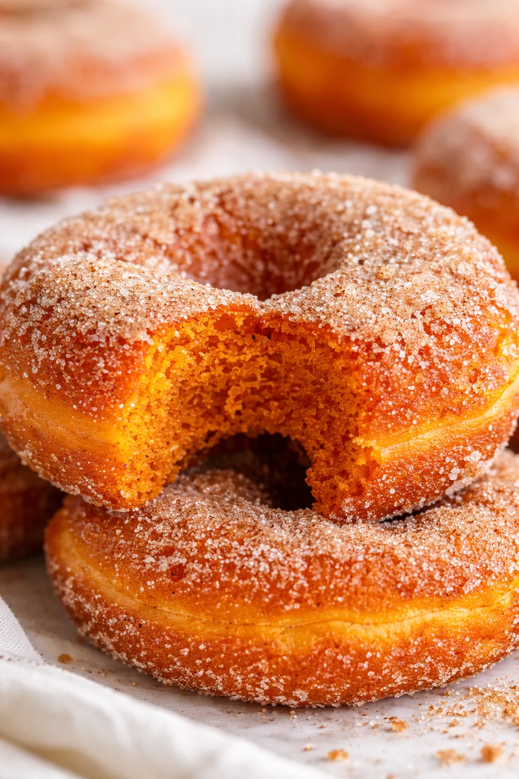 Close-up of sugar-dusted orange donuts stacked on parchment, with a soft-focus background.