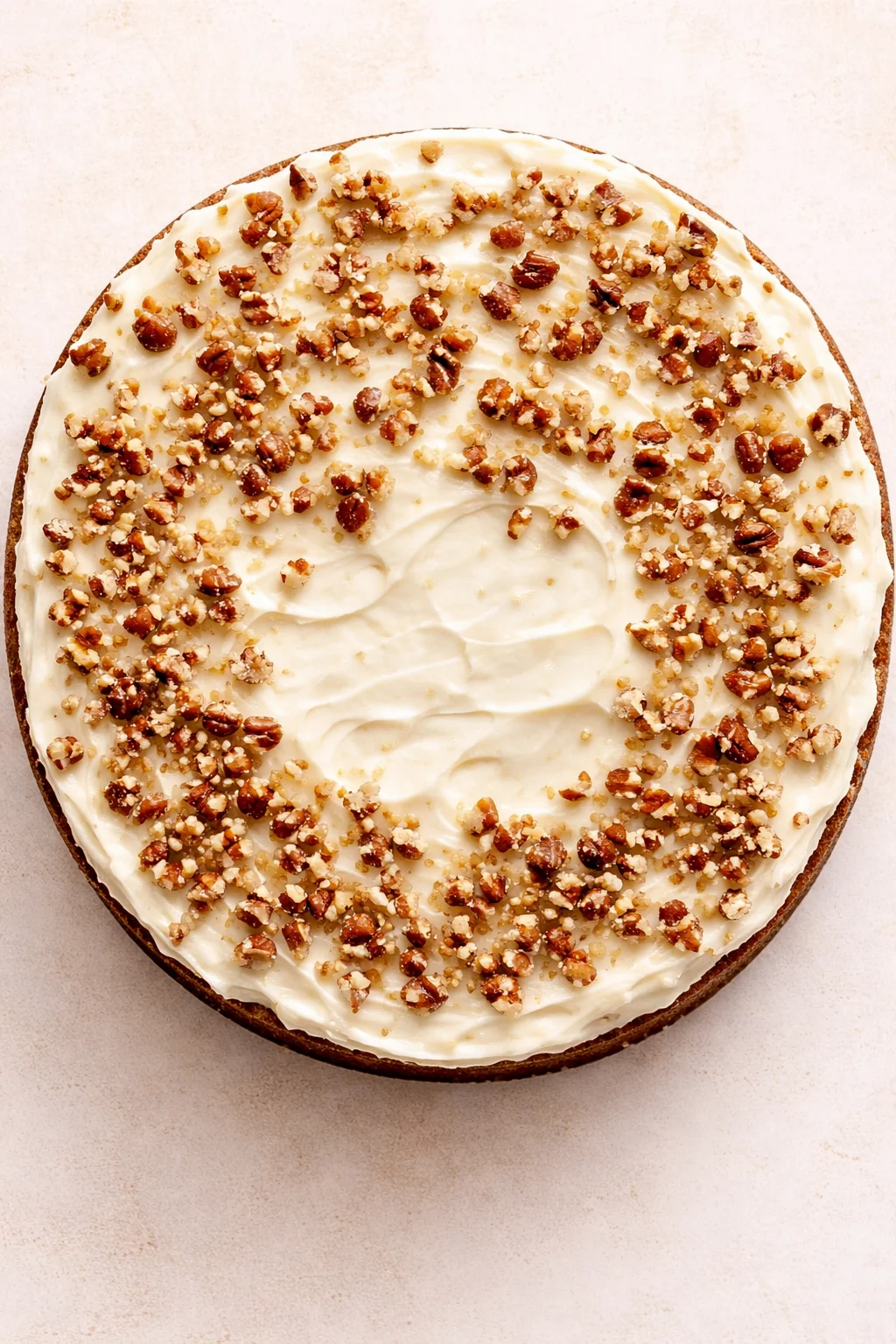 round cake with cream-cheese frosting and chopped pecans on top, viewed from above.
