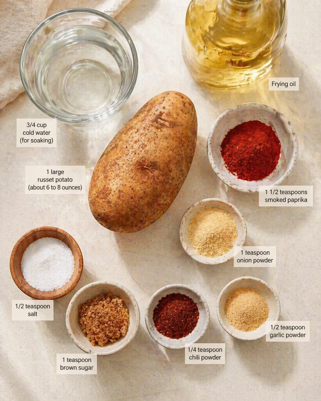 Overhead view of a russet potato with water, frying oil, and labeled spice bowls