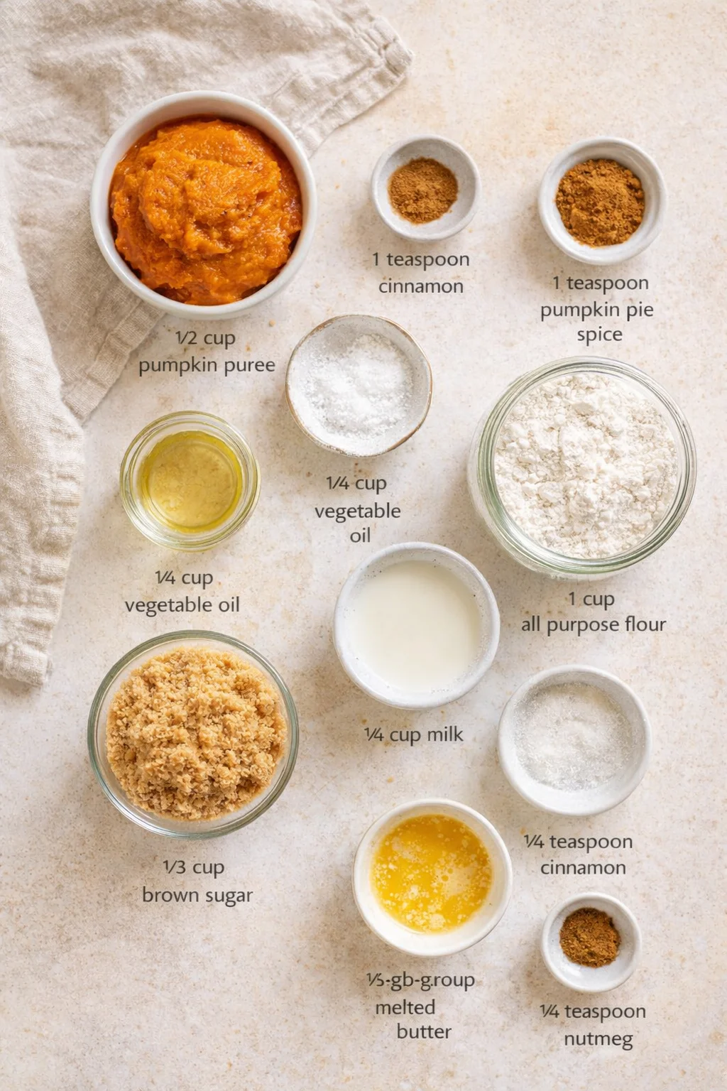 Overhead view of pumpkin puree and baking ingredients arranged on a beige surface with labeled bowls.