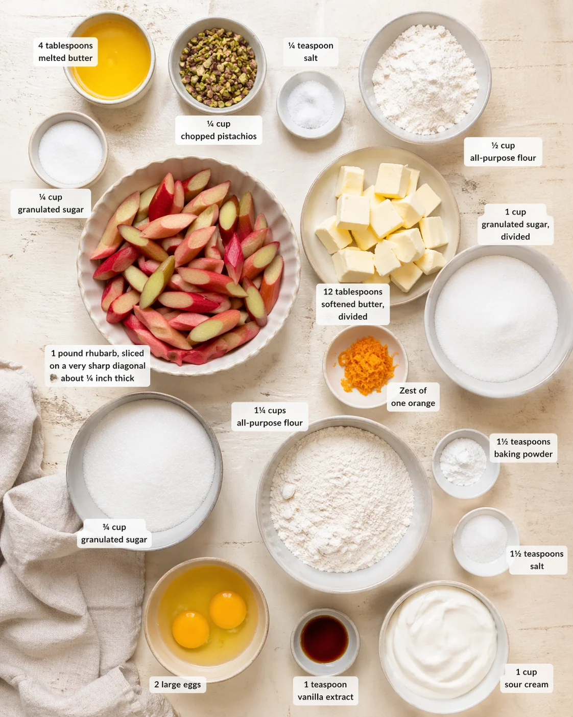 Top-down view of a baking-layout with rhubarb, pistachios, butter, flour, sugar, eggs, and orange zest.