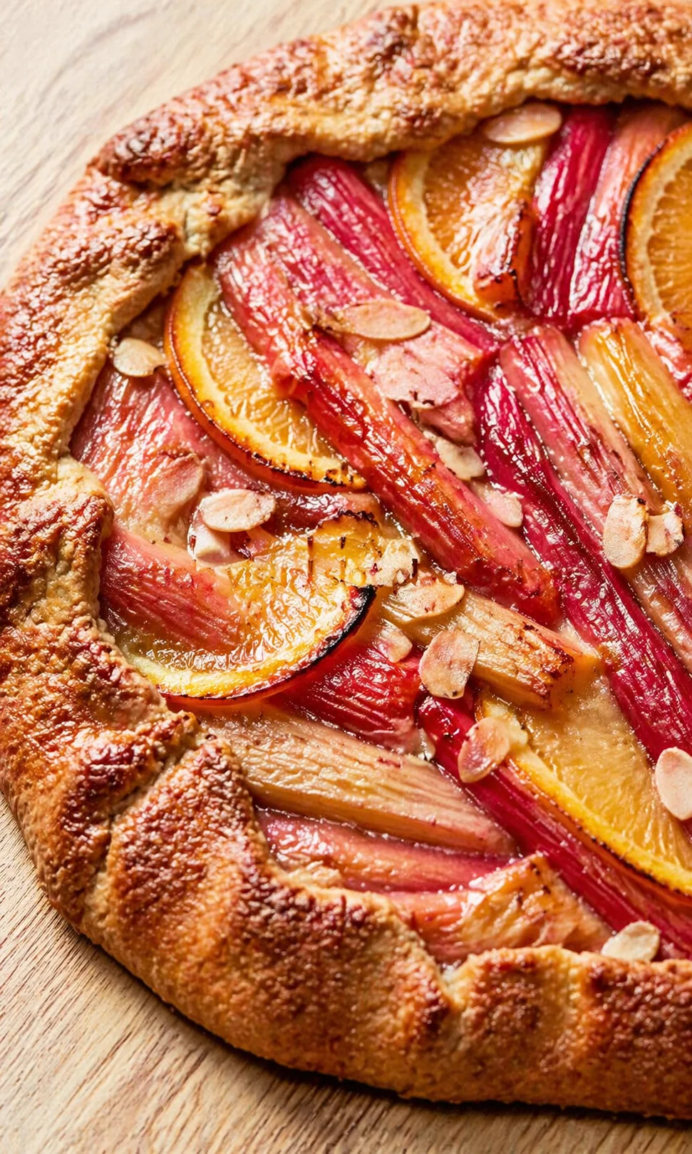Rustic fruit galette with orange slices, almond toppings, and a golden crust on a wooden board.