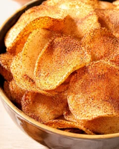 Close-up of golden brown seasoned potato chips in a brown bowl, speckled with paprika.