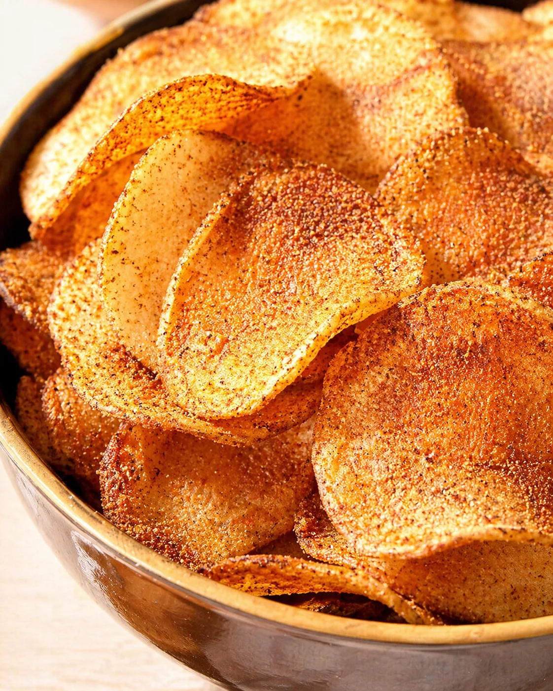 Close-up of golden brown seasoned potato chips in a brown bowl, speckled with paprika.