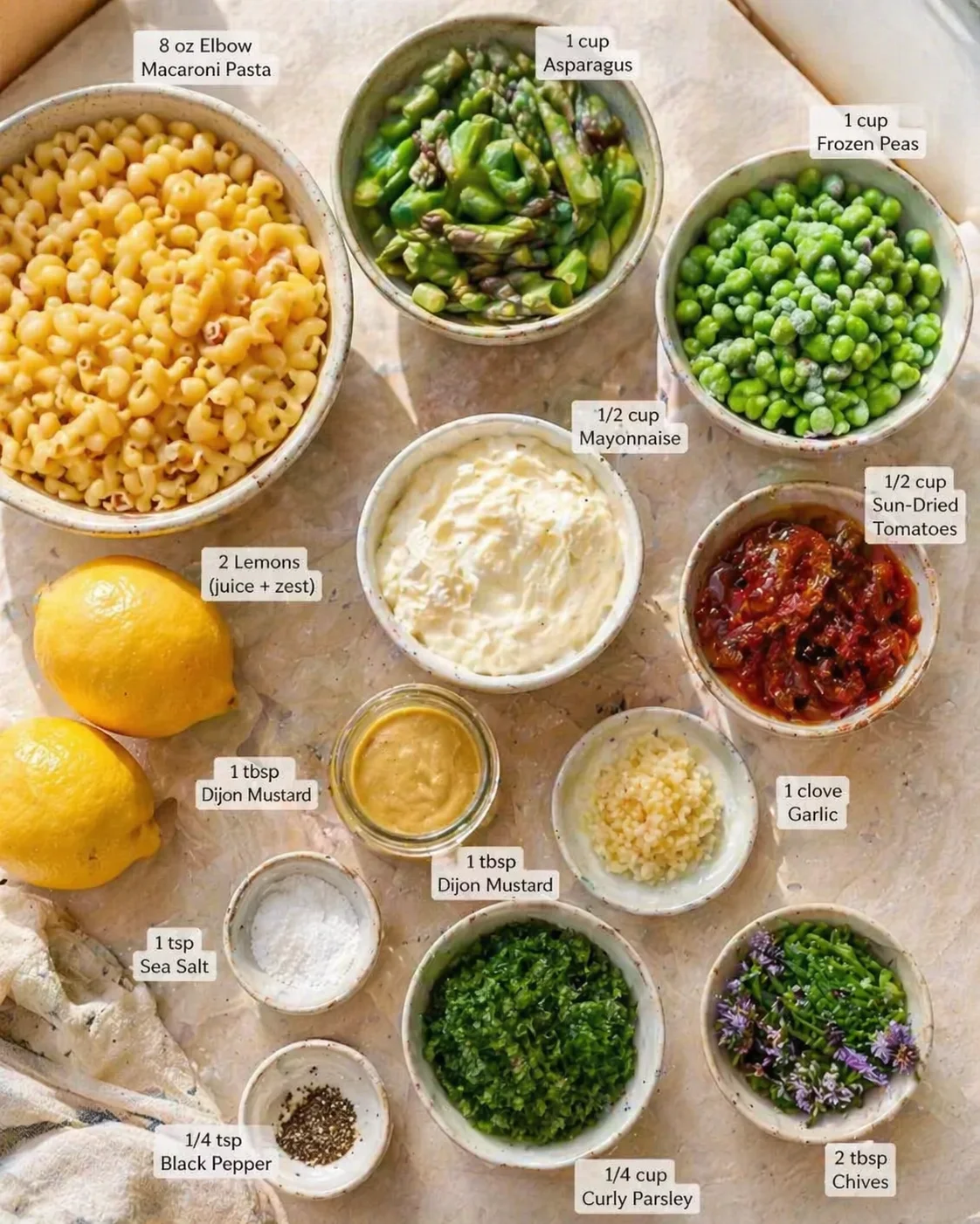 top-down view of labeled pasta salad ingredients with macaroni, asparagus, peas, sun-dried tomatoes, lemons, and sauces.