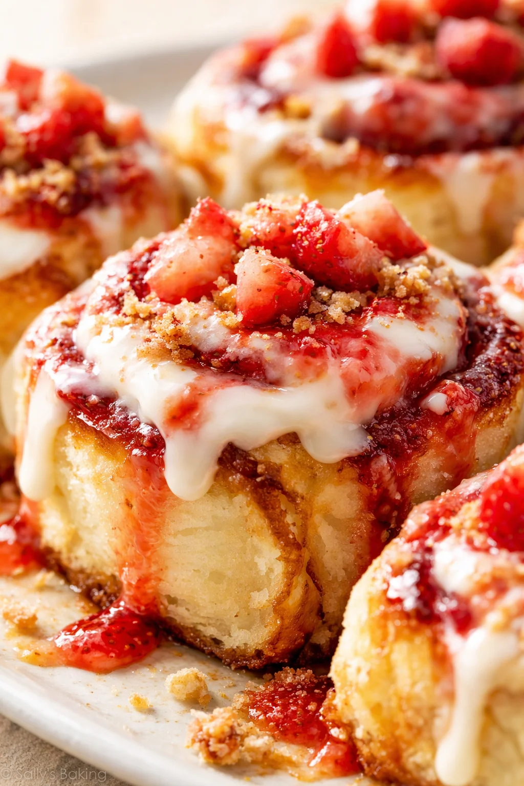 Close-up of fluffy rolls with white glaze and strawberry sauce, topped with crumb streusel.