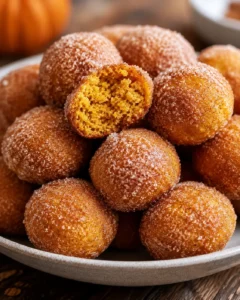 Collection of freshly baked pumpkin donut holes coated in cinnamon sugar on a white plate.