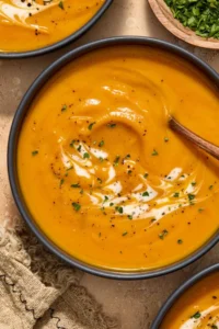 Bowl of carrot and sweet potato soup with cream and herbs swirled over top.