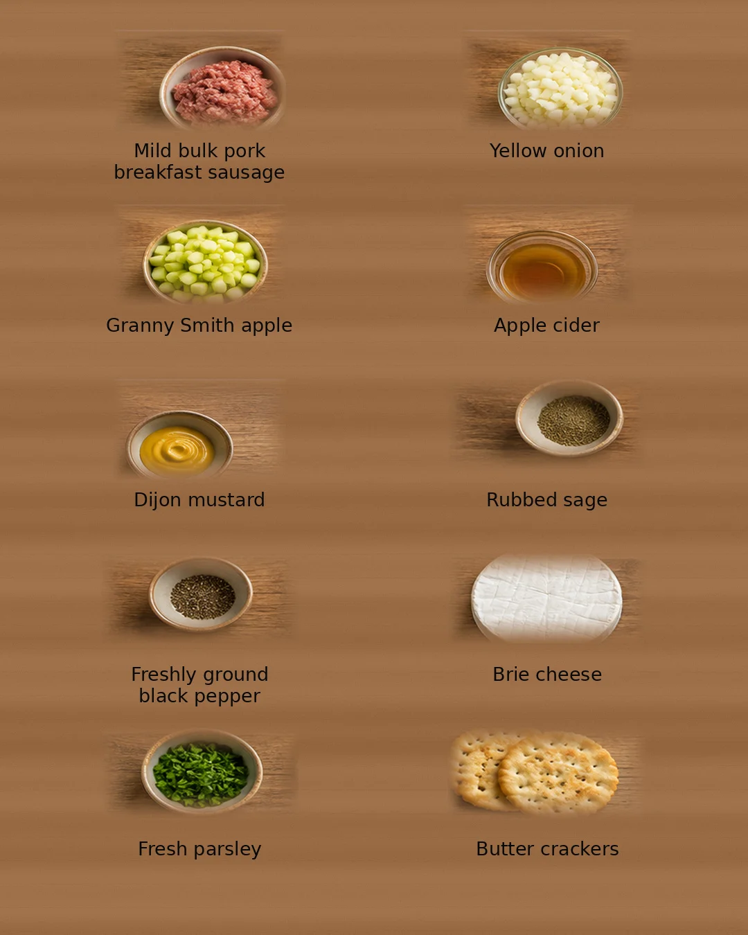 Top-down view of a wooden board with bowls of pork sausage, onion, apple, cider, mustard, sage, pepper, brie, parsley, and crackers.